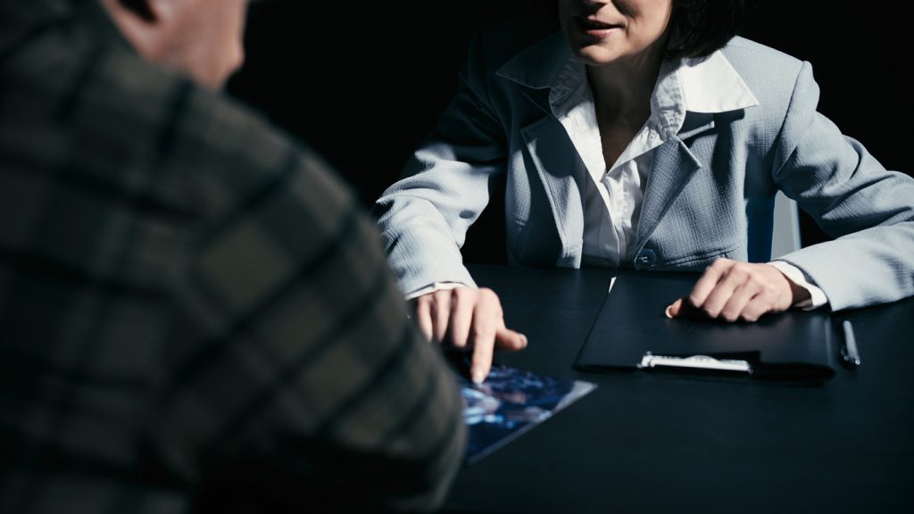 Female lawyer questioning accused man about the crime scene, showing him photos due to the initial disclosure of his case